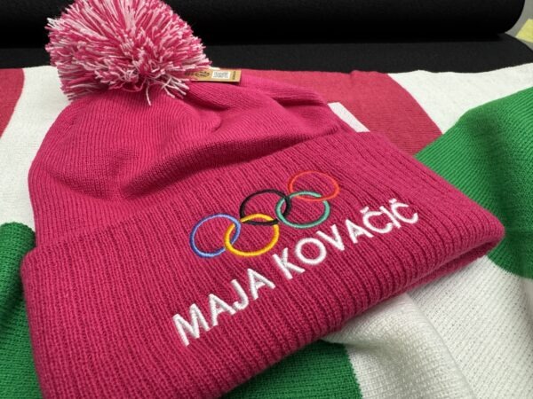 Personalizirana zimska kapa z vezenjem olimpijskih krogov in imenom Maja Kovač – kakovostno strojno vezenje na promocijskem tekstilu za športne ekipe in navijače.