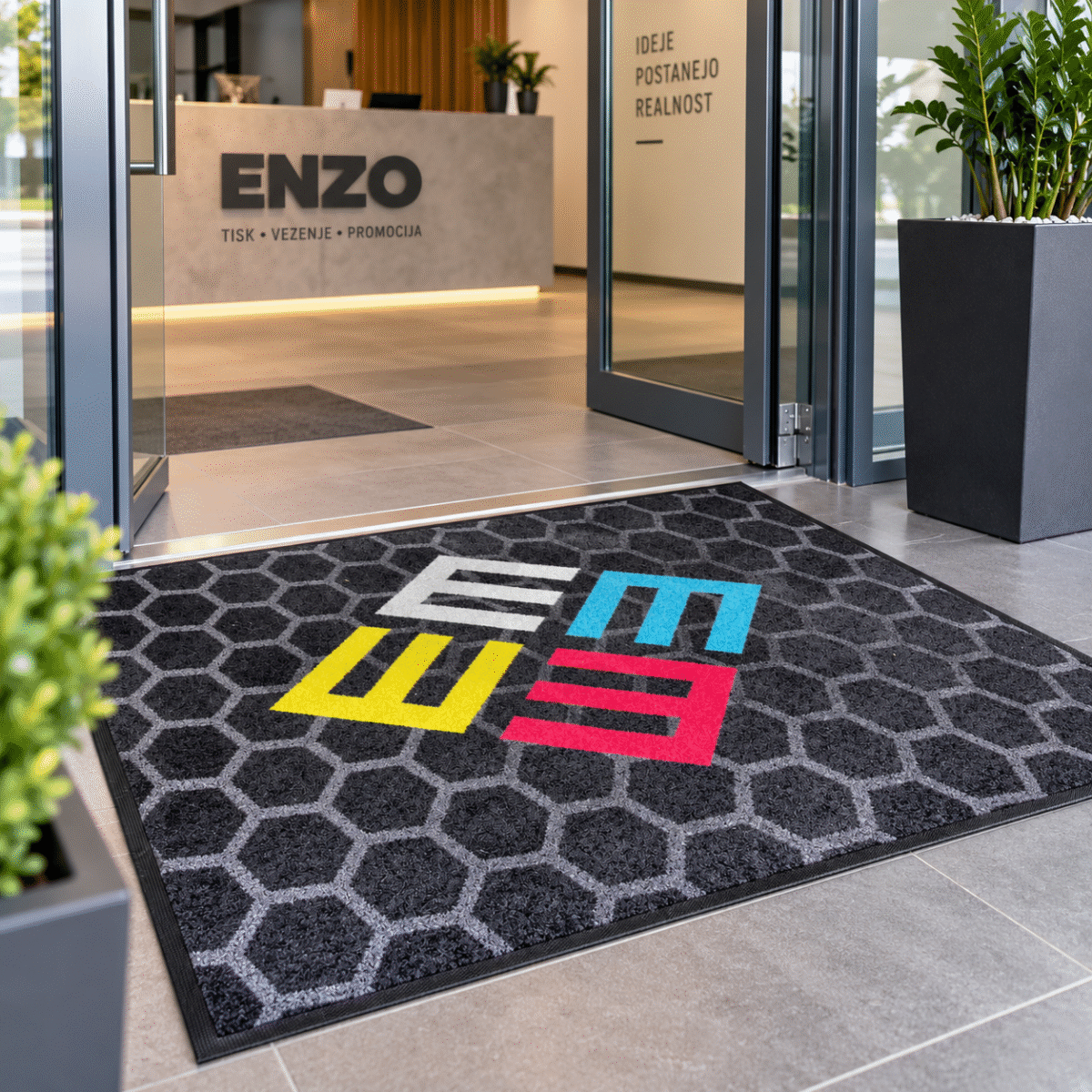 Predpražnik z logotipom ENZO po meri v sodobnem poslovnem vhodu – personaliziran predpražnik za podjetja z barvnim logotipom in nedrsečo gumijasto podlago.